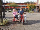 Zwei Kinder fahren auf einem roten Dreirad.