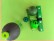 ein gemaltes grünes Chamäleon versteckt sich zwischen verschiedenen grünen Gegenständen 