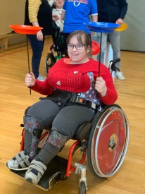 Mädchen im Rollstuhl balanciert auf beiden Händen Jonglierteller