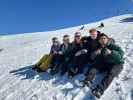 Eine Gruppe von Jugendlichen sitzt im Schnee vor blauen Himmel