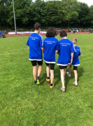 Vier Schüler:innen von hinten fotografiert in blauen Triktos auf einem Fußballplatz